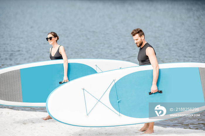 Beautiful couple in black swimwear walking with standup paddleboard on the beach ready for surfing