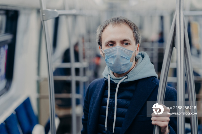 Photo of male passenger wears face mask while travels by subway during infectious disease, prevents spreading coronavirus, poses in public transport, thinks about epidemic situation in his country