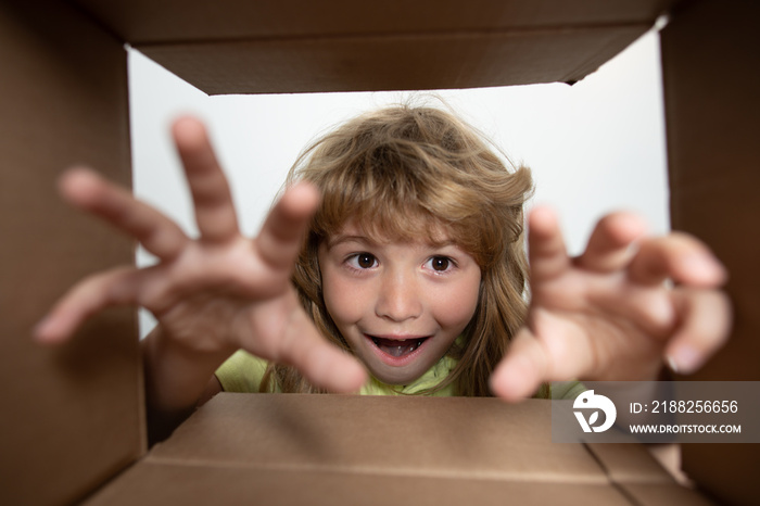 Funny excited child unpacking and opening the carton box looking inside. The little kids unboxing gift inside view. Child boy looking surprised into a gift.