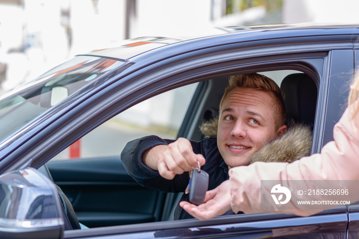 Smiling young man in a car handing over his keys