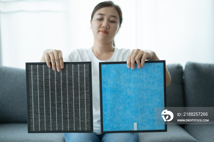 Beautiful Asian young woman holding a HEPA carbon air purifier filter in living room.