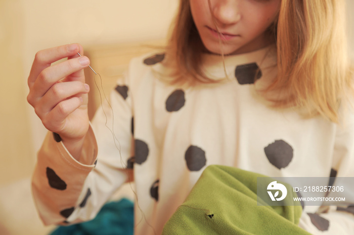 Female child hands hold a needle with a thread and some clothes to mend it. Sustainable consumption, ecology, recycle, sustainability, reusing, concept.