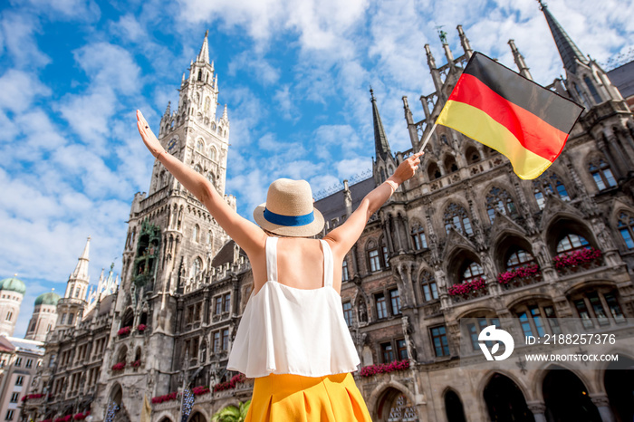 Young female tourist with raised hands holding german flag on the central square in front of the town hall building in Munich