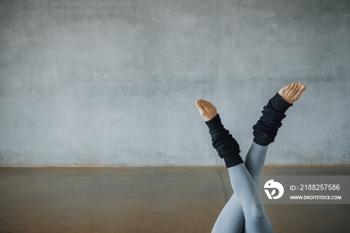 Close up detailed shot of female feet barefoot, crossed, up side down, in yoga pose, with leg warmers, at a industrial concrete wall of a modern urban gymnasium. Copy-space, Horizontal.