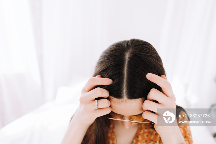 Young brunette woman showing her scalp, hair roots, color, brunette hair, hair loss or dry scalp problem.