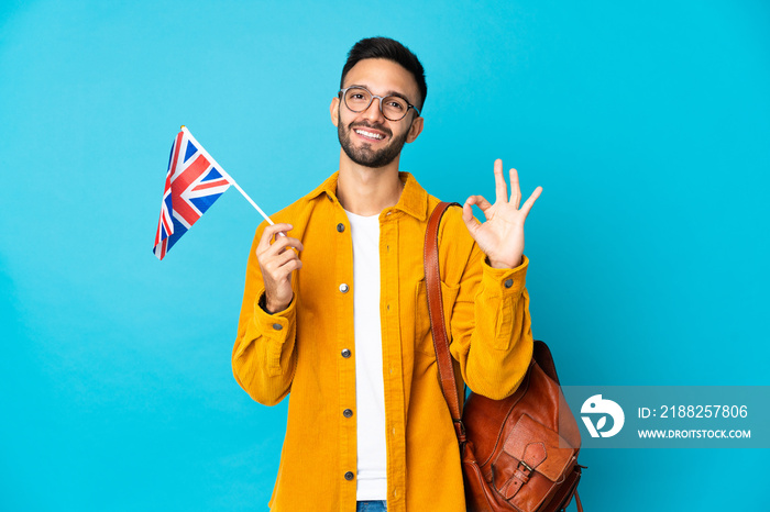 Young caucasian man holding an United Kingdom flag isolated on yellow background showing ok sign with fingers