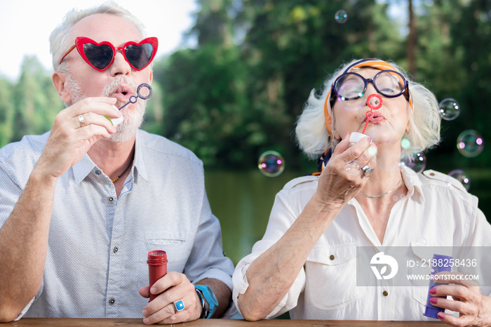 Blowing bubbles. Active funny aged couple standing together and blowing soap bubbles