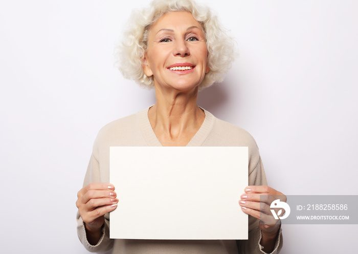 Portrait of happy senior woman with blank advertising board or copy space, over light grey background, close up