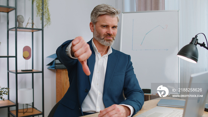 Dislike. Upset mature businessman working on laptop computer at home office thumbs down sign gesture, expressing discontent, disapproval, dissatisfied bad work. Displeased serious freelancer old man