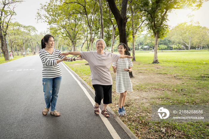 Asian granddaughter,daughter assisting senior mother to walking follow white line on the floor with the support at park, female elderly try to balance with arms open,testing and risk fall prevention