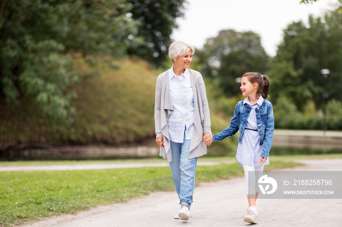 family, leisure and people concept - happy grandmother and granddaughter walking at summer park