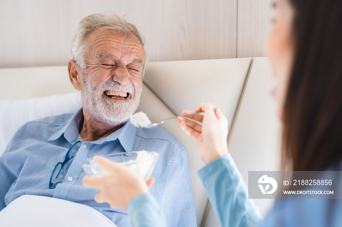 Elderly patient having support health care service by nurse in a old people home providing residential care by bringing breakfast to her senior man occupant, medical care of retirement caucasian man