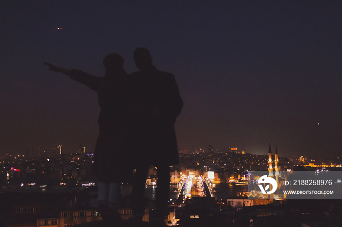 Couple on Valide Han roof. Illuminated lights of night Istanbul view