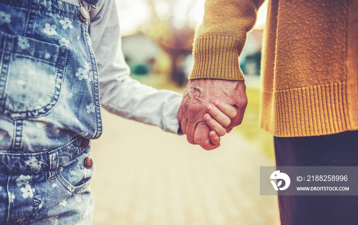 Two generations. Old woman and little child holding hands while walking together, close up photo. Family, lifestyle concept