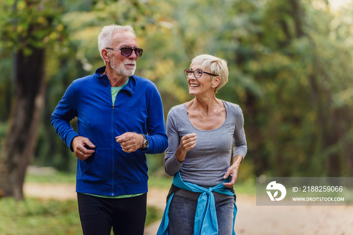 Cheerful active senior couple jogging in the park. Exercise together to stop aging.