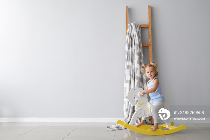 Adorable baby girl with rocking horse near light wall