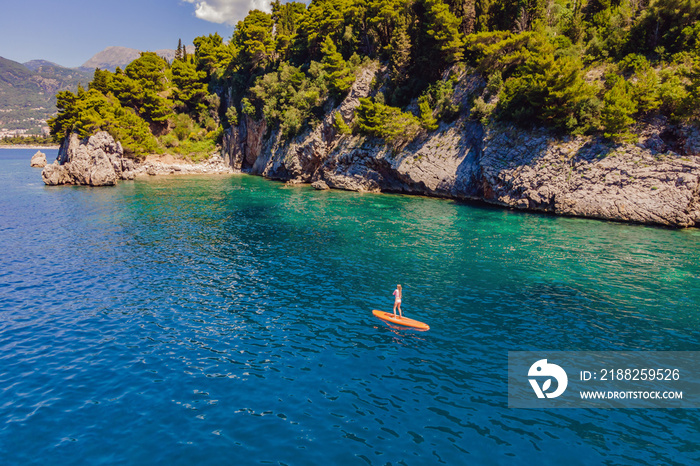 Young women Having Fun Stand Up Paddling in blue water sea in Montenegro. SUP. girl Training on Paddle Board near the rocks