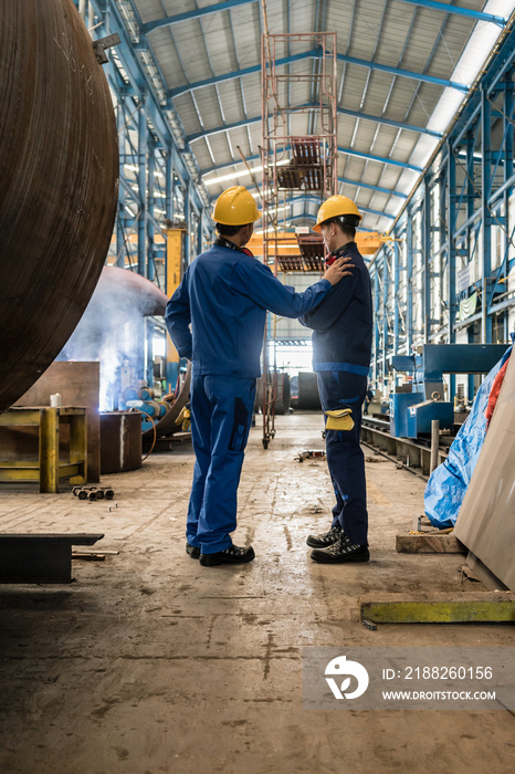 Two workers wearing yellow hard hat and blue uniform in the interior of an industrial hall