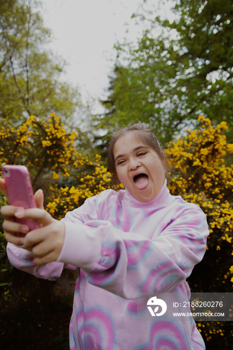 Curvy girl with Down Syndrome taking a goofy selfie in the park