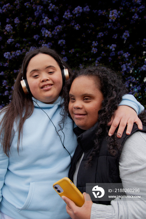 Two curvy women with Down Syndrome hugging in front of flowers