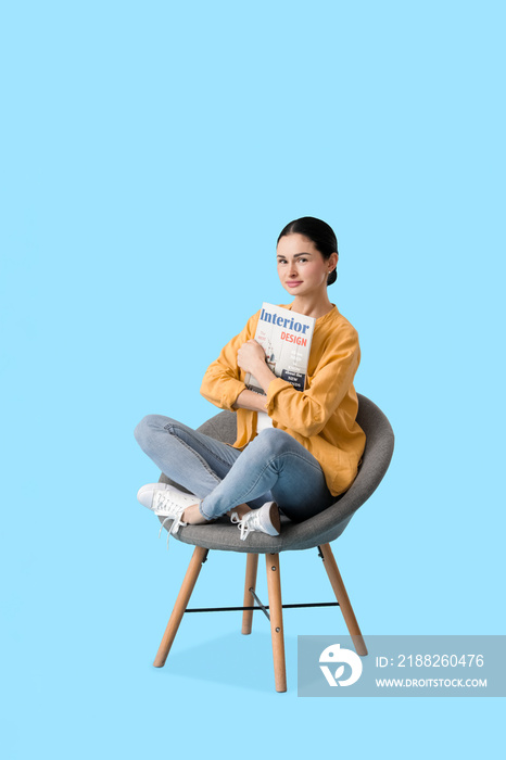 Beautiful young woman with magazine sitting in armchair on color background