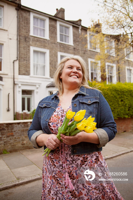 Portrait of happy plus-sized woman holding flowers in an urban environment