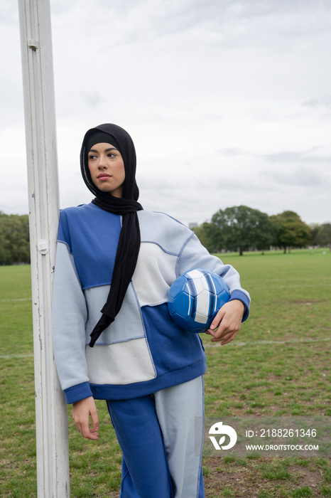 Portrait of woman in hijab standing in soccer field with soccer ball