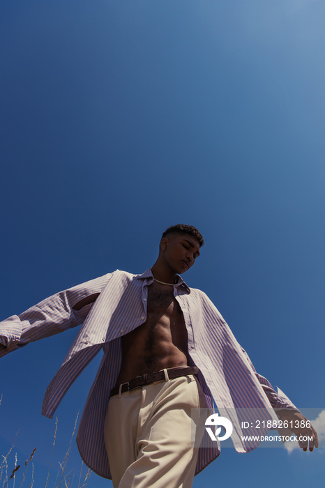 low angle view of african american man in striped shirt and white trousers against cloudless sky