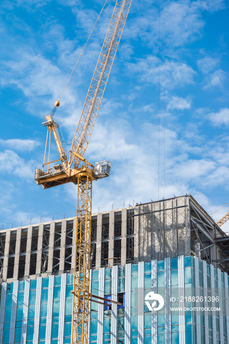 Tower crane in modern office building construction site with blue sky background. Construction industry concept.