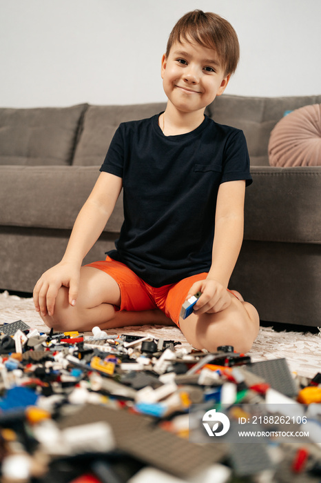 Smiling boy playing lego at home on the floor. First education role lifestyle