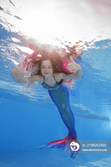 A girl in a mermaid costume poses underwater in a pool