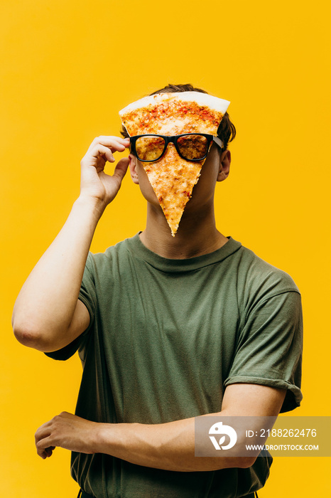 The pizza man. A guy with a piece of pizza on his face poses on a colored background. Creative concept of pizza advertising.