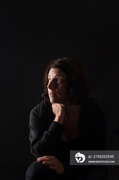 portrait of a woman sitting and look up on black background