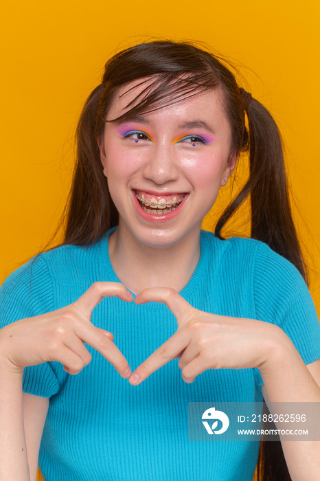 Studio portrait of girl with colorful make-up showing heart shaped gesture