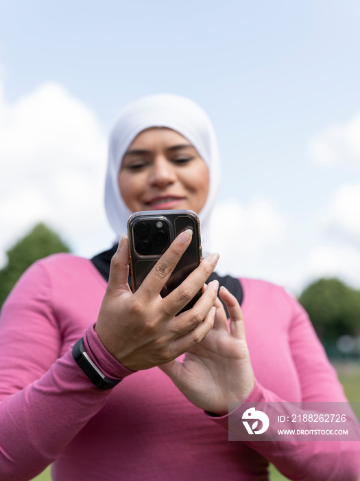 UK,Sutton,Woman in headscarf holding smart phone in park