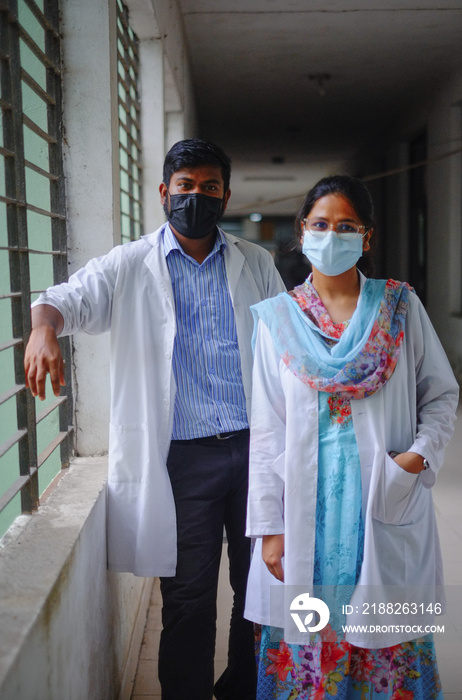 South asian medical student in hospital corridor wearing white apron and face mask