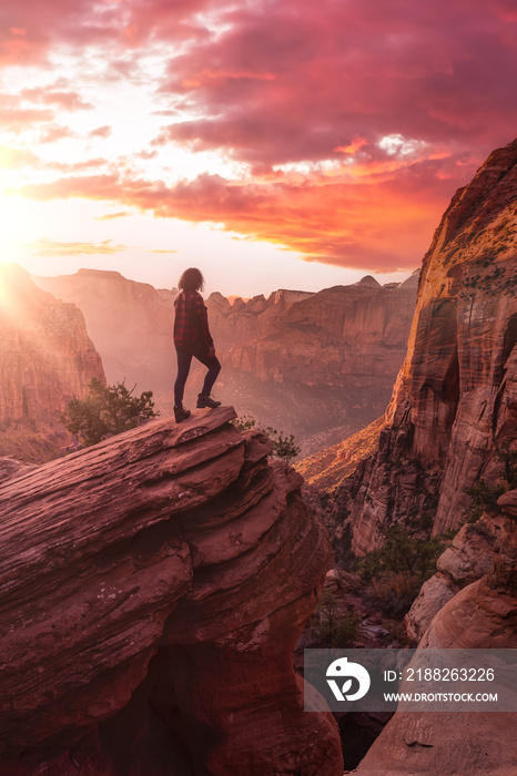 Adventurous Woman at the edge of a cliff is looking at a beautiful landscape view in the Canyon. Sunset Sky Art Render. Taken in Zion National Park, Utah, United States.