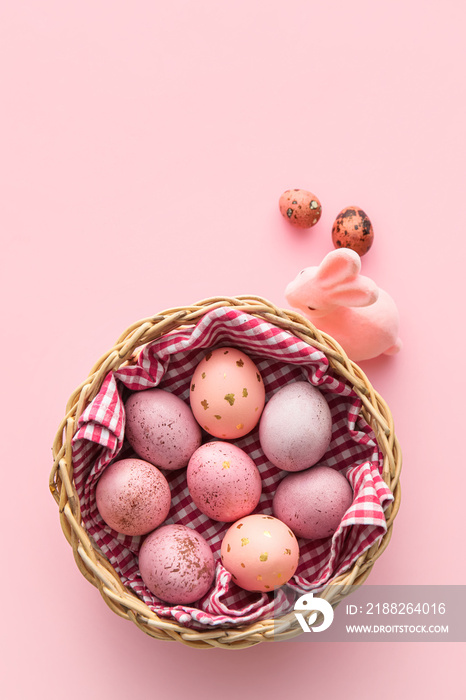 Basket with painted Easter eggs and bunny on pink background