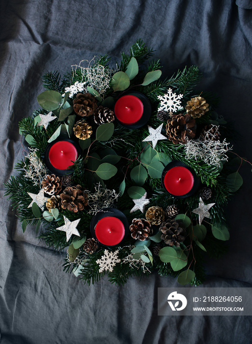 Christmas composition of advent wreath on dark grey table linen background. Made of evergreen fir tree branches, eucalyptus leaves, snowflakes, golden and natural pine cones. Flat lay, top view.