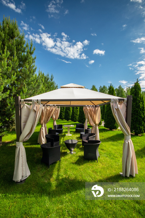 White canvas gazebo with plastic garden furniture in a summer green lawn. Vertical, copy space.