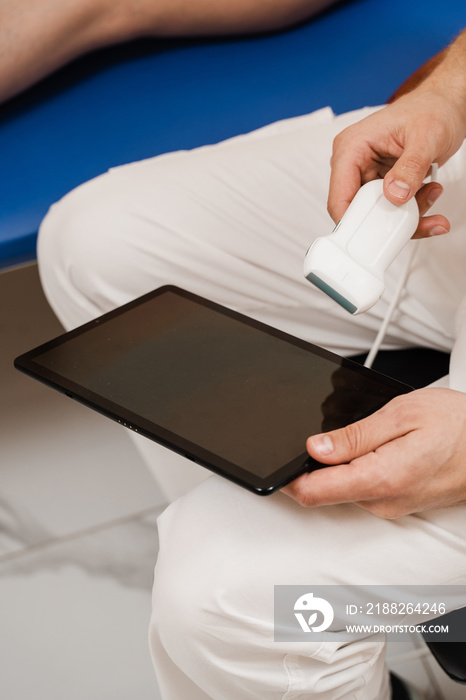 Portable ultrasound machine for ultrasound legs scanning. Vascular surgeon examines veins and arteries of legs using ultrasound machine of woman in medical clinic.