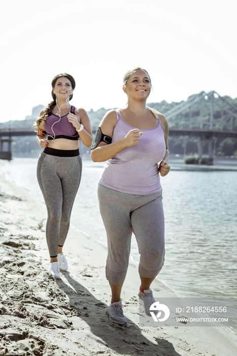Cardio activity. Happy active women enjoying their training while jogging near the river