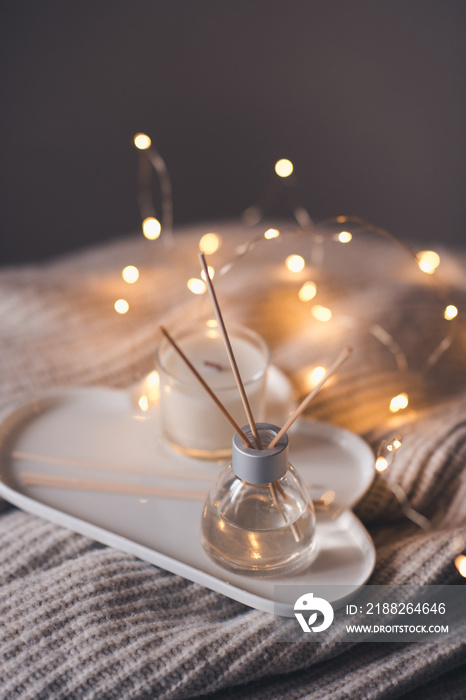 Home liquid perfume in glass bottle with bamboo sticks and scented candle on tray at coffee table in room. Cozy atmosphere.