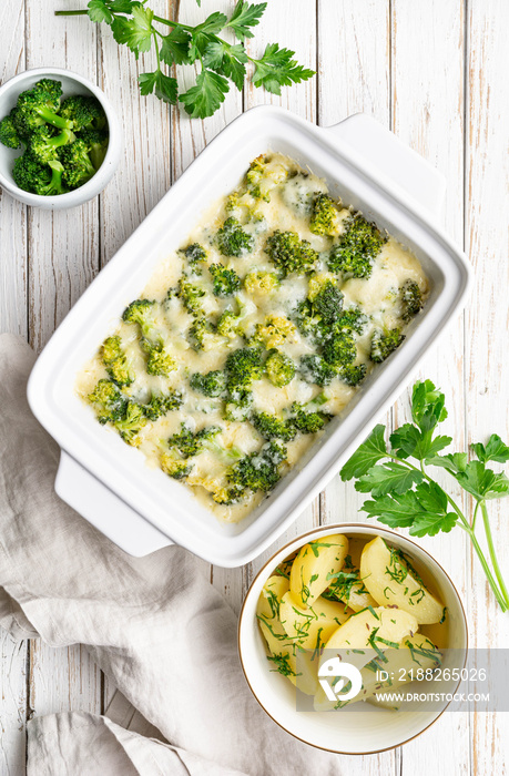 Broccoli and cheese casserole served with boiled potatoes on white wooden background