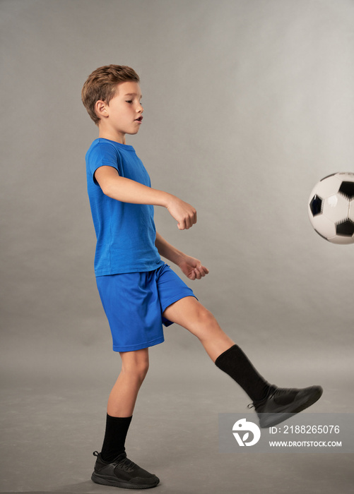 Little football player kicking the ball against gray background