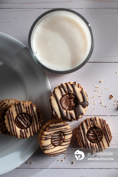 Vanilla cookies stuffed with cream chocolate on a white plate over a white wooden table and a glass of ice milk on the side, vertical top view overhead or flat lay shot