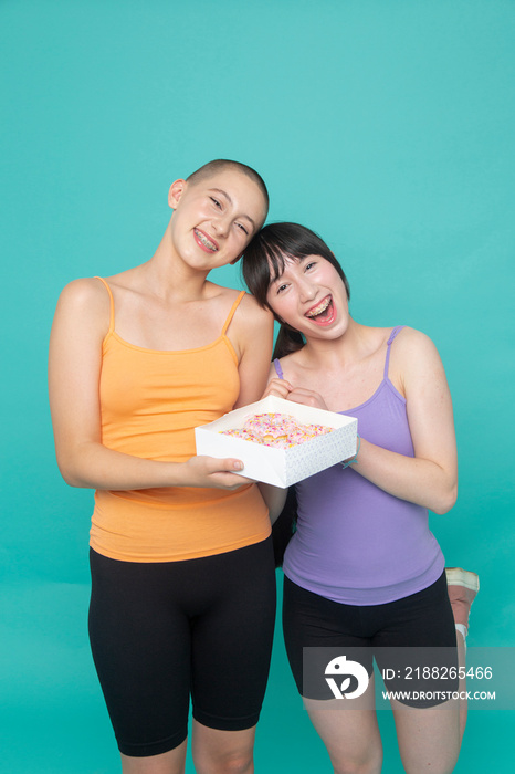 Studio portrait of smiling friends holding box of donuts