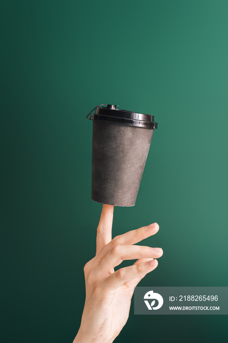 Dark cup on the index finger against green background.