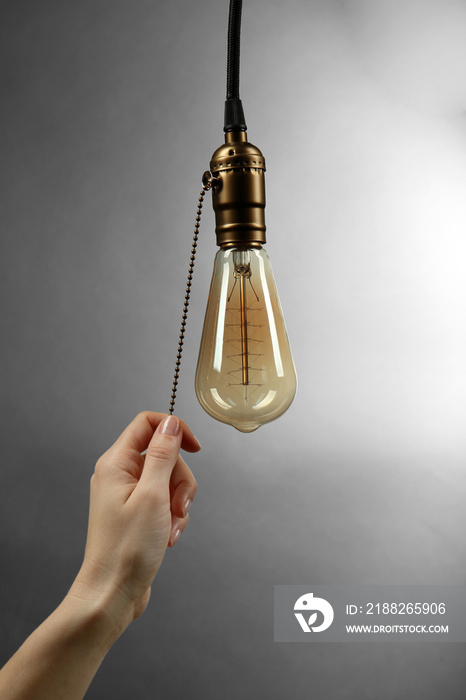 Female hand turning on light bulb on  grey background