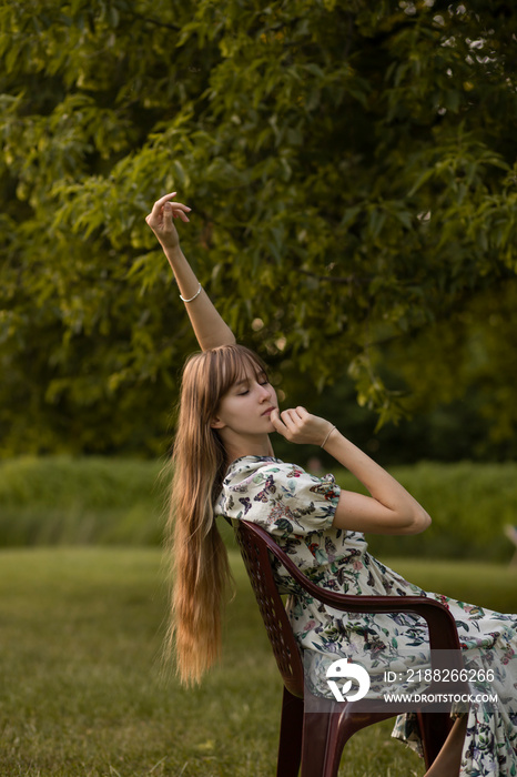 woman in a park sits on a chair in the forest with long blond hair. tender aesthetic girls